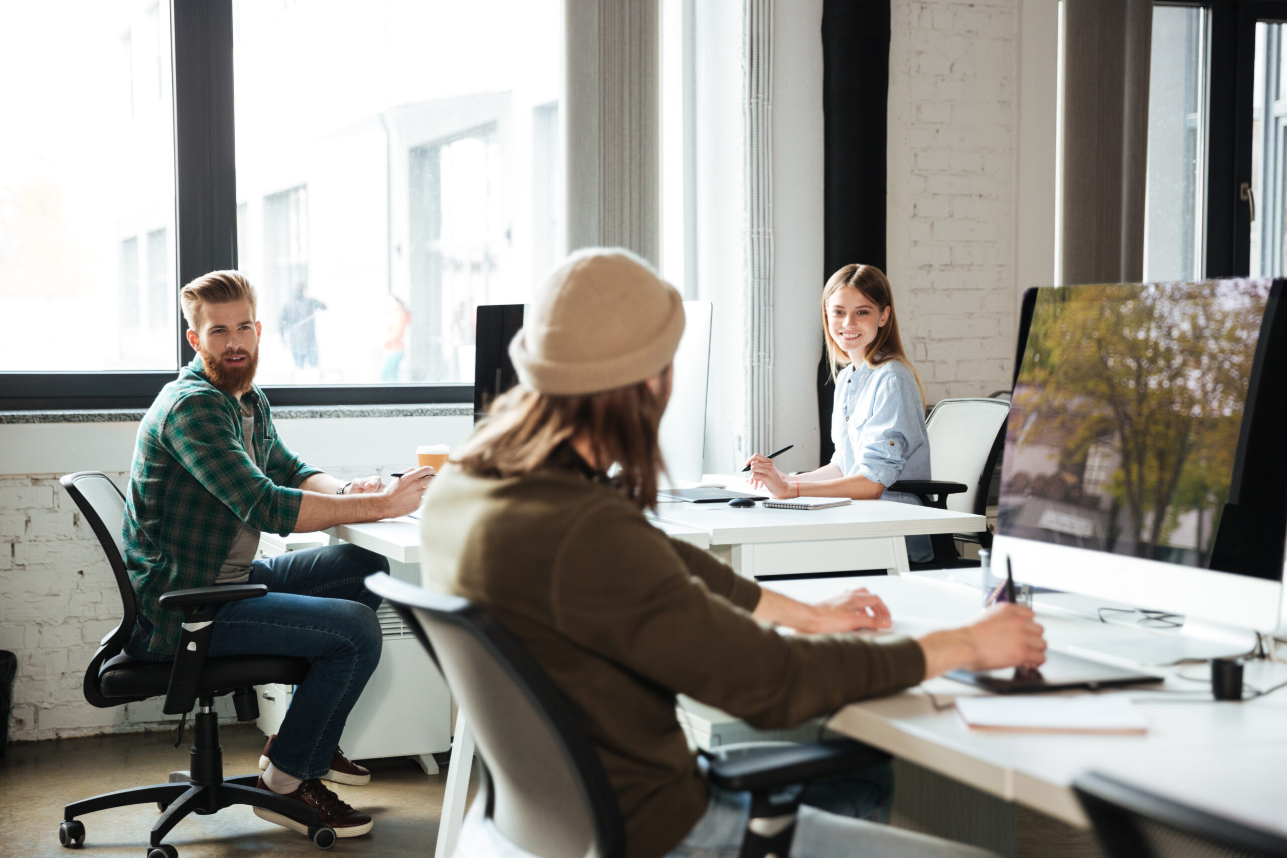 Picture of young colleagues work in office using computers. Looking aside.