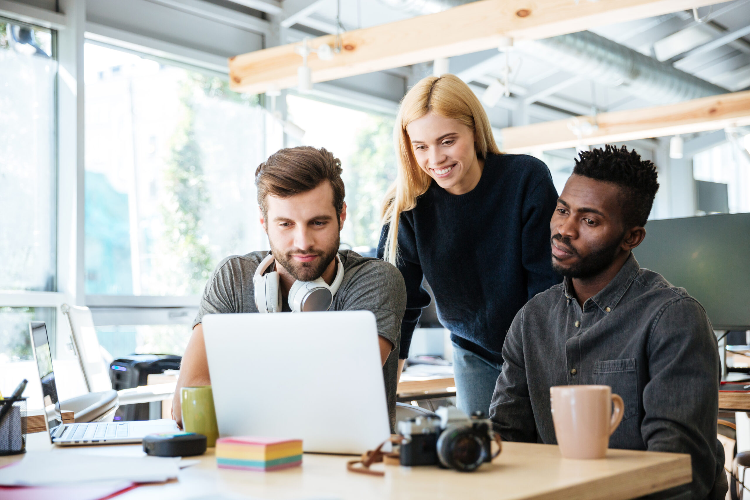 Photo of young smiling colleagues sitting in office coworking. Looking aside talking with each other.